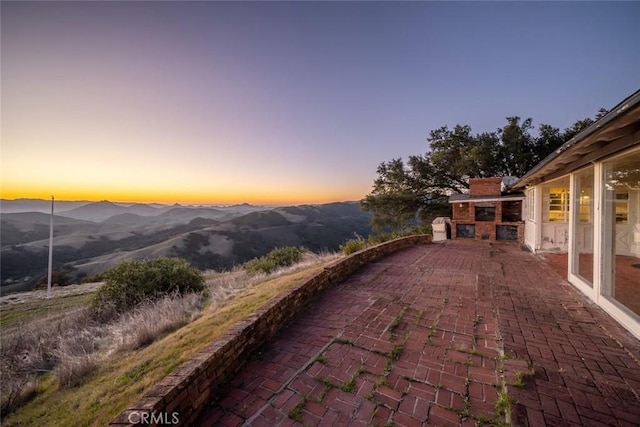 patio terrace at dusk with a fireplace and a mountain view