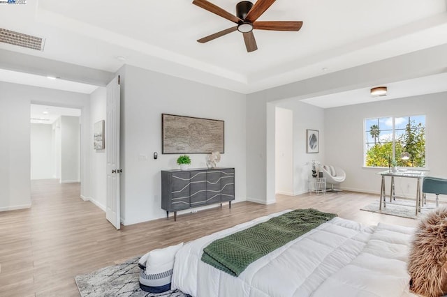 bedroom featuring ceiling fan, a tray ceiling, and light hardwood / wood-style flooring