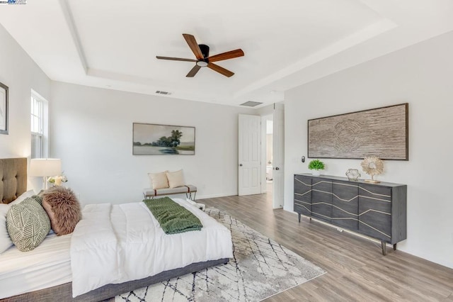 bedroom with ceiling fan, hardwood / wood-style floors, and a tray ceiling