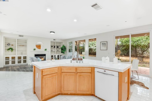 kitchen with tile countertops, a kitchen island with sink, dishwasher, a wealth of natural light, and sink