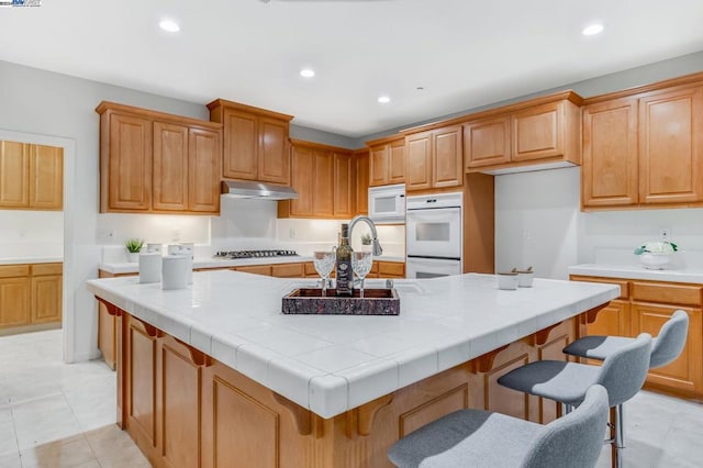 kitchen featuring light tile patterned floors, a breakfast bar area, tile counters, white appliances, and a kitchen island