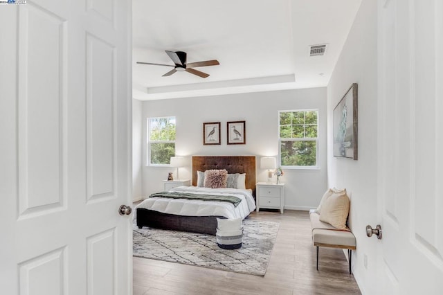 bedroom with ceiling fan, a raised ceiling, and multiple windows