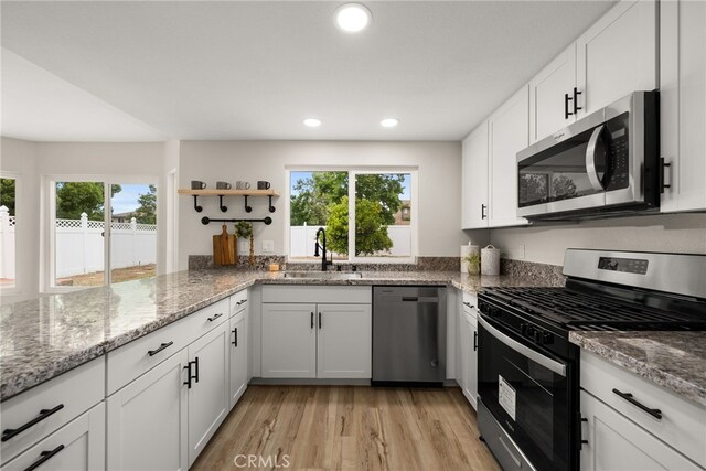 kitchen with appliances with stainless steel finishes, white cabinetry, light stone counters, and sink