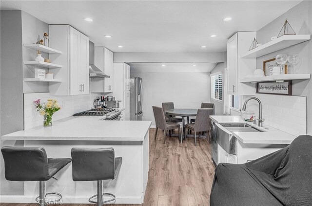 kitchen featuring tasteful backsplash, kitchen peninsula, wall chimney exhaust hood, and white cabinetry