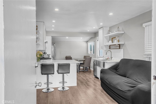 kitchen with white cabinetry, stainless steel fridge, kitchen peninsula, light wood-type flooring, and a breakfast bar area