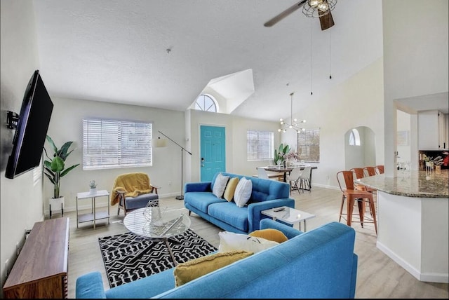 living room with ceiling fan with notable chandelier, light hardwood / wood-style floors, and vaulted ceiling