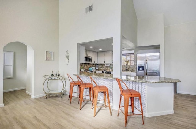 kitchen with a kitchen bar, kitchen peninsula, appliances with stainless steel finishes, a high ceiling, and light stone countertops