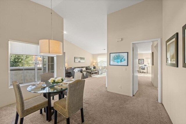 dining area featuring high vaulted ceiling and light colored carpet