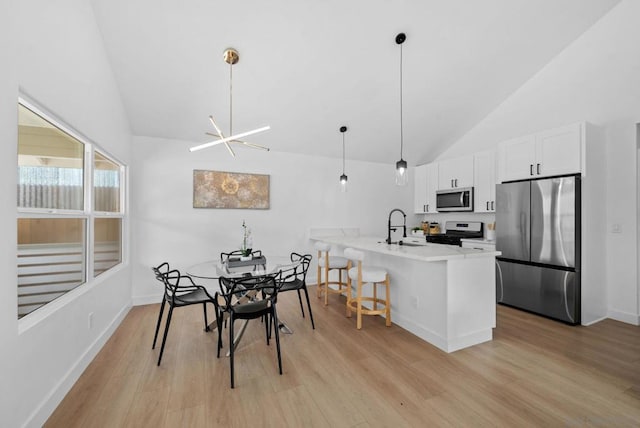 kitchen with a breakfast bar, white cabinetry, hanging light fixtures, light wood-type flooring, and appliances with stainless steel finishes