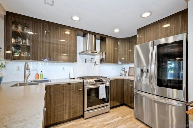 kitchen with appliances with stainless steel finishes, wall chimney exhaust hood, light hardwood / wood-style floors, and sink