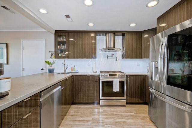 kitchen with appliances with stainless steel finishes, light wood-type flooring, wall chimney range hood, crown molding, and sink