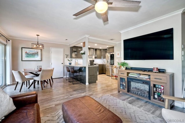 living room with sink, crown molding, a chandelier, and light hardwood / wood-style floors