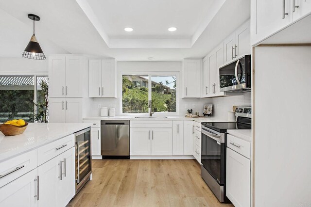 kitchen with white cabinetry, appliances with stainless steel finishes, a tray ceiling, wine cooler, and pendant lighting