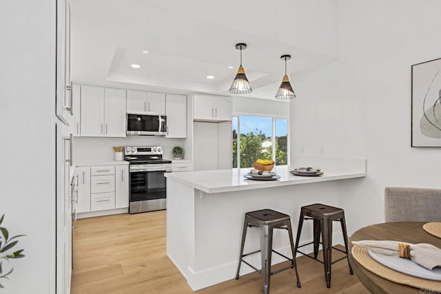 kitchen with appliances with stainless steel finishes, white cabinetry, tasteful backsplash, light hardwood / wood-style floors, and a breakfast bar