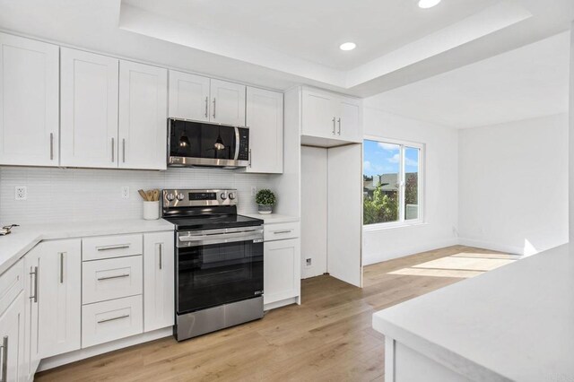 kitchen featuring tasteful backsplash, a raised ceiling, light hardwood / wood-style flooring, stainless steel appliances, and white cabinets