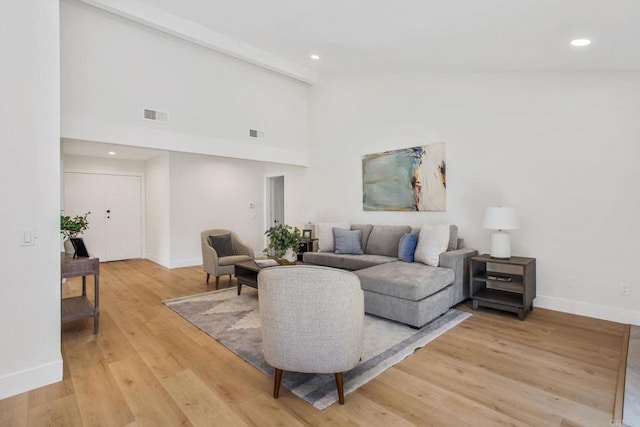 living room with beam ceiling, a high ceiling, and light hardwood / wood-style floors