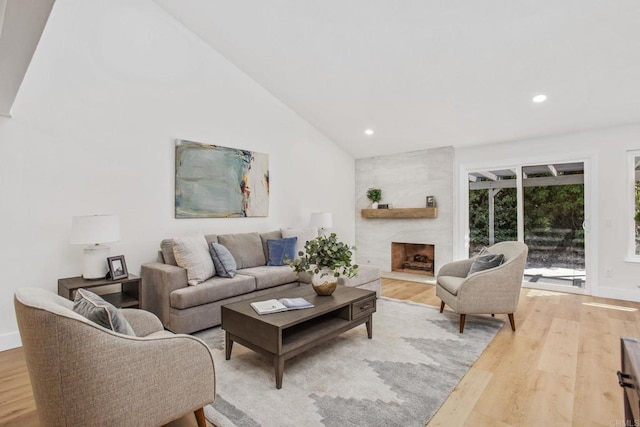 living room with vaulted ceiling, a large fireplace, and light hardwood / wood-style floors