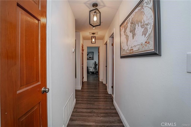 corridor with dark wood-type flooring, visible vents, and baseboards