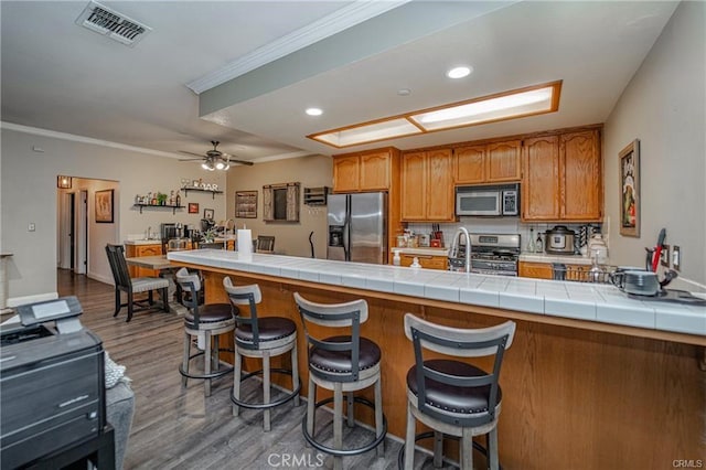 kitchen with a sink, wood finished floors, visible vents, appliances with stainless steel finishes, and brown cabinetry