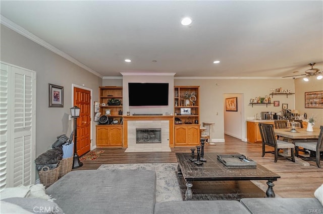 living area featuring crown molding, recessed lighting, a tiled fireplace, wood finished floors, and baseboards