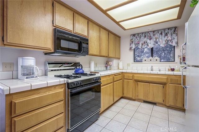 kitchen featuring sink, tile counters, gas stove, and light tile patterned flooring