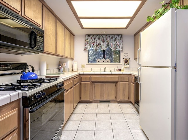 kitchen with white fridge, light tile patterned floors, tile counters, range with gas stovetop, and sink