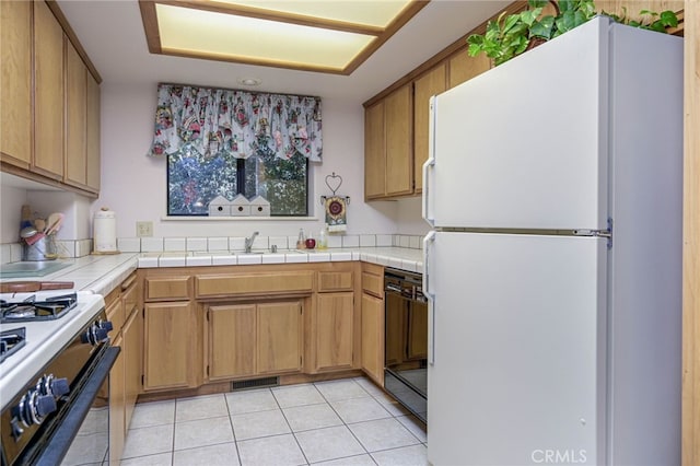 kitchen featuring dishwasher, white fridge, tile countertops, light tile patterned flooring, and stove