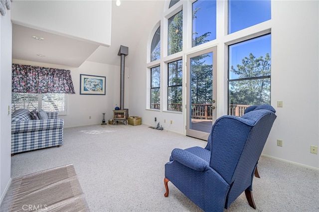 living area featuring carpet floors, a towering ceiling, and a wood stove