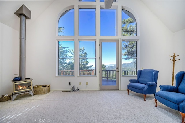 living area featuring light colored carpet, a wood stove, and high vaulted ceiling