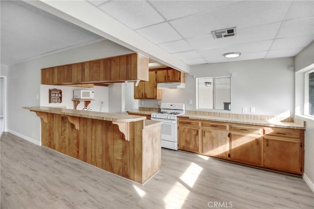 kitchen featuring white appliances, a paneled ceiling, a kitchen bar, kitchen peninsula, and light wood-type flooring