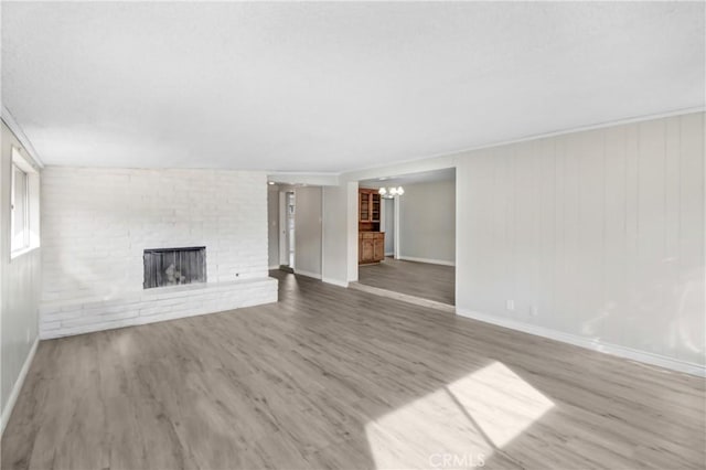 unfurnished living room with wood-type flooring, a fireplace, ornamental molding, and a notable chandelier