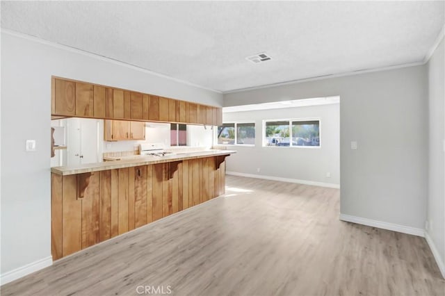 kitchen featuring stove, kitchen peninsula, a kitchen bar, crown molding, and light hardwood / wood-style flooring