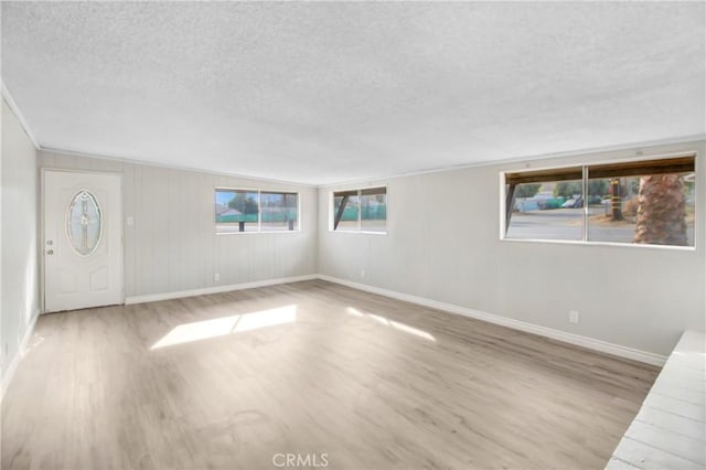 empty room with light wood-type flooring, a textured ceiling, and ornamental molding