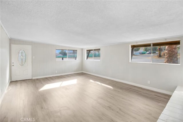 empty room featuring light wood-type flooring, crown molding, and a textured ceiling