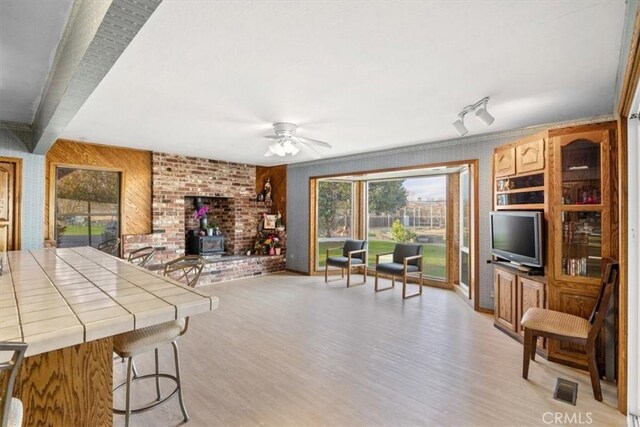 living room featuring light wood-type flooring, ceiling fan, a wood stove, and wooden walls