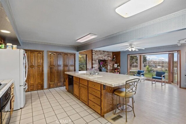 kitchen with black appliances, a kitchen bar, sink, tile countertops, and crown molding