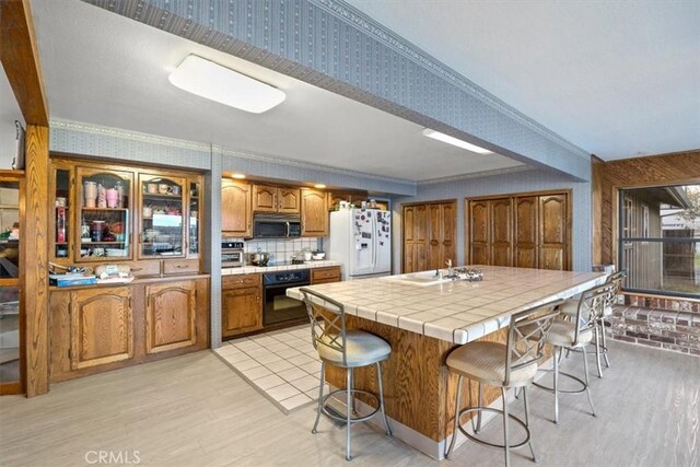 kitchen featuring tile countertops, black appliances, a kitchen bar, sink, and ornamental molding