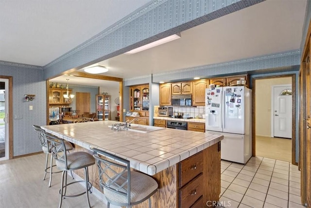 kitchen with oven, a sink, white fridge with ice dispenser, wallpapered walls, and tile counters