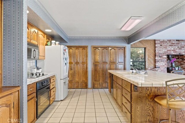 kitchen featuring light tile patterned floors, tile countertops, crown molding, and black appliances