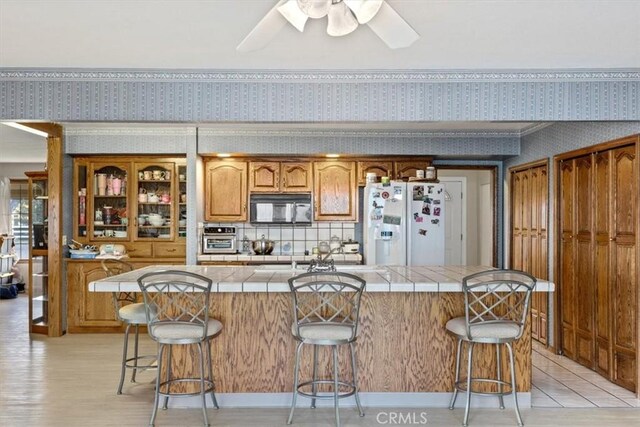 kitchen with white fridge with ice dispenser, a center island, a kitchen bar, tile countertops, and ceiling fan