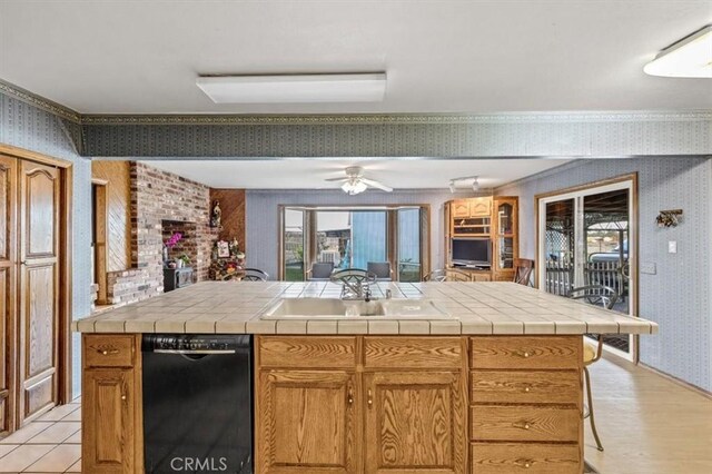 kitchen featuring tile counters, ceiling fan, black dishwasher, and a kitchen bar