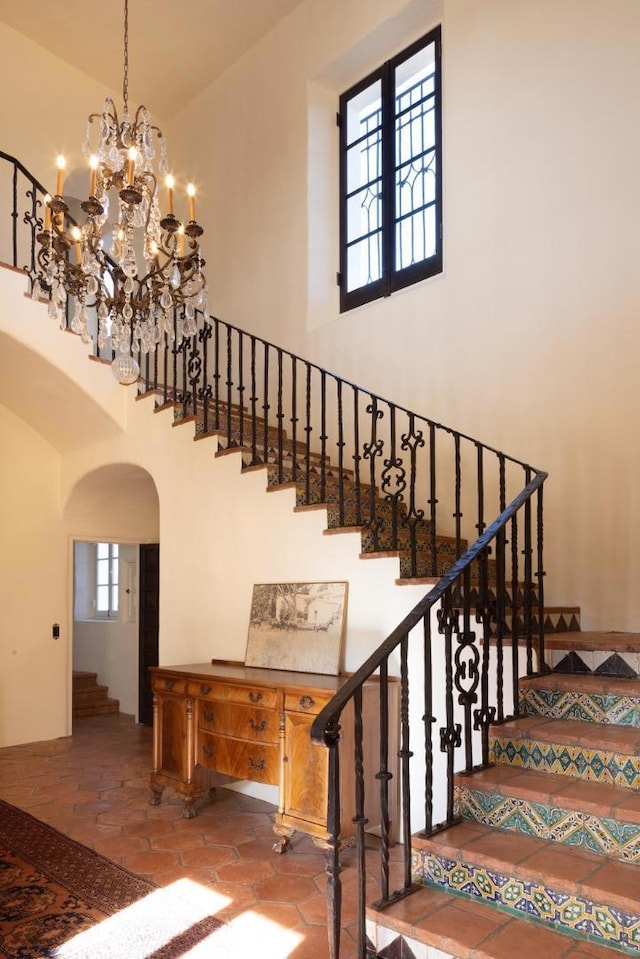 staircase with tile patterned flooring, a notable chandelier, and a towering ceiling