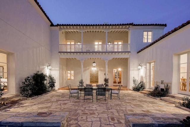 back house at dusk featuring a patio area and a balcony