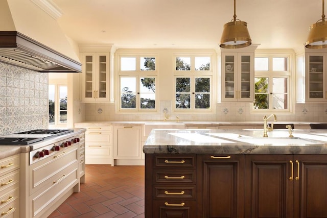 kitchen with stainless steel gas stovetop, premium range hood, backsplash, pendant lighting, and sink