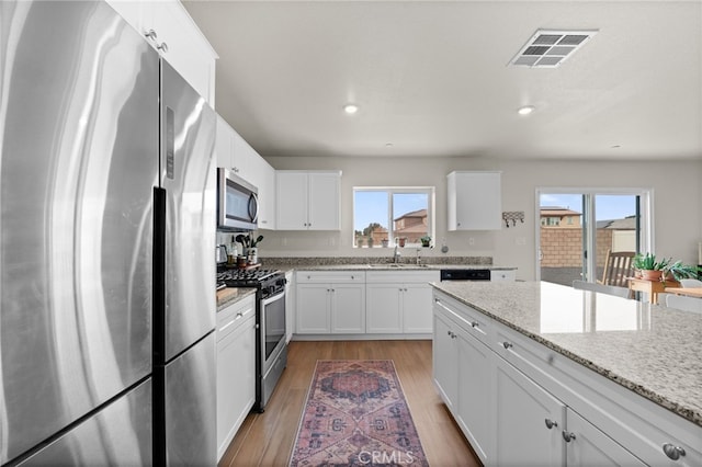 kitchen with a wealth of natural light, appliances with stainless steel finishes, white cabinetry, sink, and light stone counters