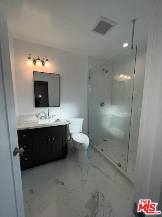 bathroom with vanity, tiled shower, and toilet