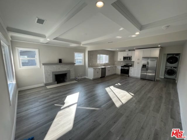 unfurnished living room featuring dark wood-type flooring, stacked washing maching and dryer, and beamed ceiling