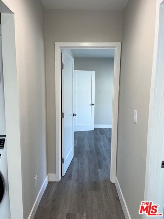 corridor with dark hardwood / wood-style flooring and stacked washing maching and dryer