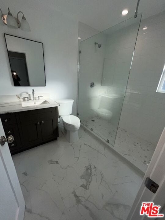 bathroom with tiled shower, vanity, and toilet