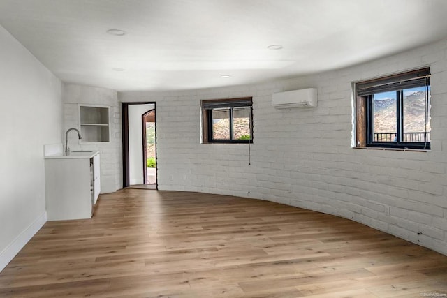 unfurnished room featuring light hardwood / wood-style floors, brick wall, sink, and a wall unit AC